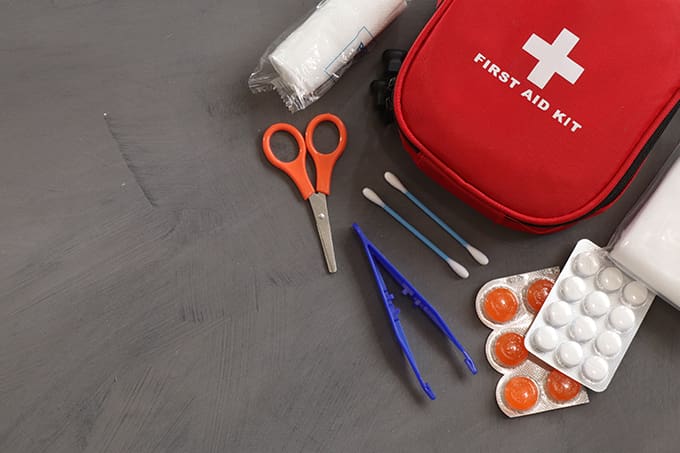 A red first aid kit with scissors, bandaids and other items.