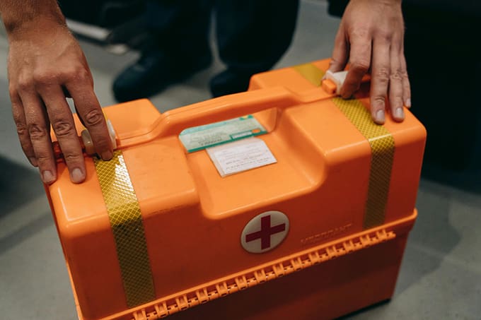 A person holding onto the handle of an orange first aid kit.